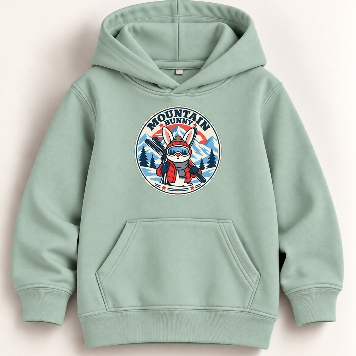 A sage green pullover hoodie with a front kangaroo pocket and a circular graphic on the chest featuring a cartoon character in ski gear with the text 'MOUNTAIN OUTDOOR'.