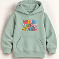 A sage green pullover hoodie with a colorful retro graphic on the chest that reads 'WILD AND FREE' in bubble letters with daisy flowers, shown against a light beige background.