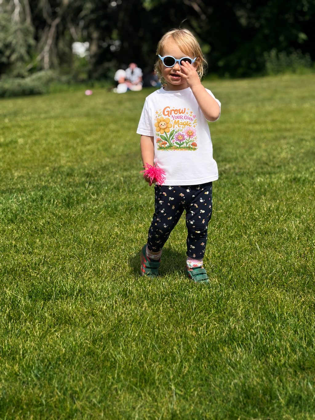 Child in a white t-shirt with a colorful design standing on grass