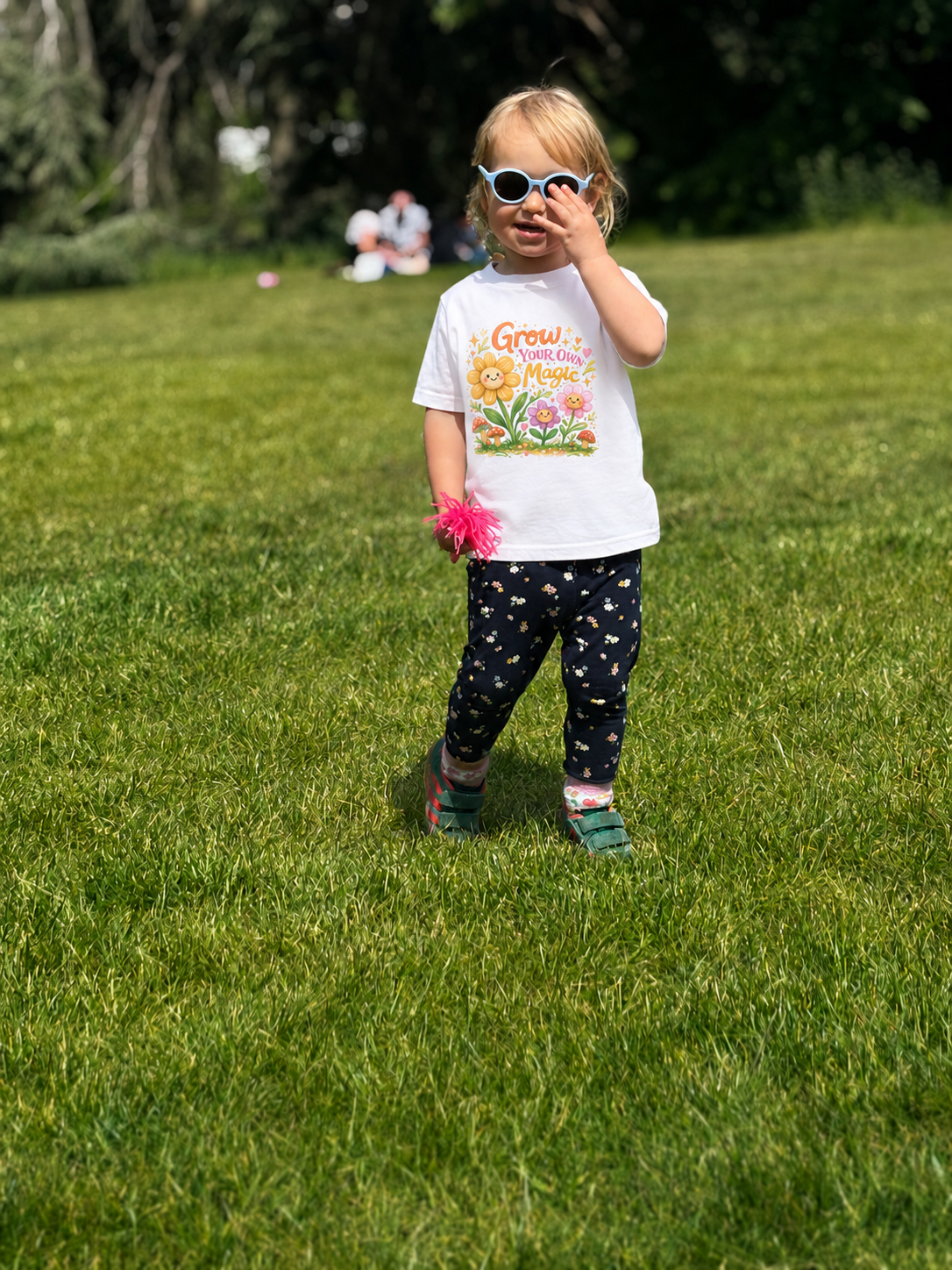 Child in a white t-shirt with a colorful design standing on grass