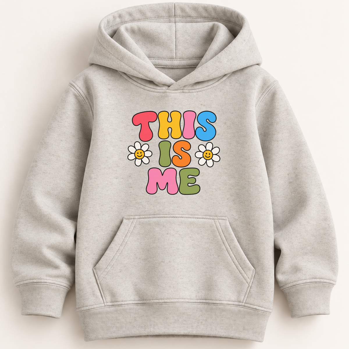 A light heather gray pullover hoodie with a colorful retro-style graphic on the chest that reads 'THIS IS ME' in multicolored letters, accented with two white daisy flowers. The hoodie is shown flat against a light beige background.