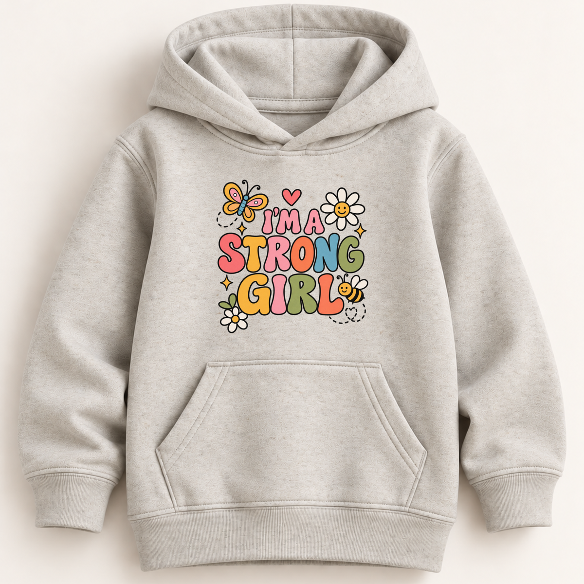 A light heather gray pullover hoodie with a colorful graphic on the chest that reads 'I'M A STRONG GIRL' in playful multicolor letters, surrounded by flowers, a butterfly, and a bee. The hoodie is shown against a plain, light beige background.