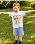 Child wearing a t-shirt with a banana character and 'Weekend Energy' text, standing on grass.