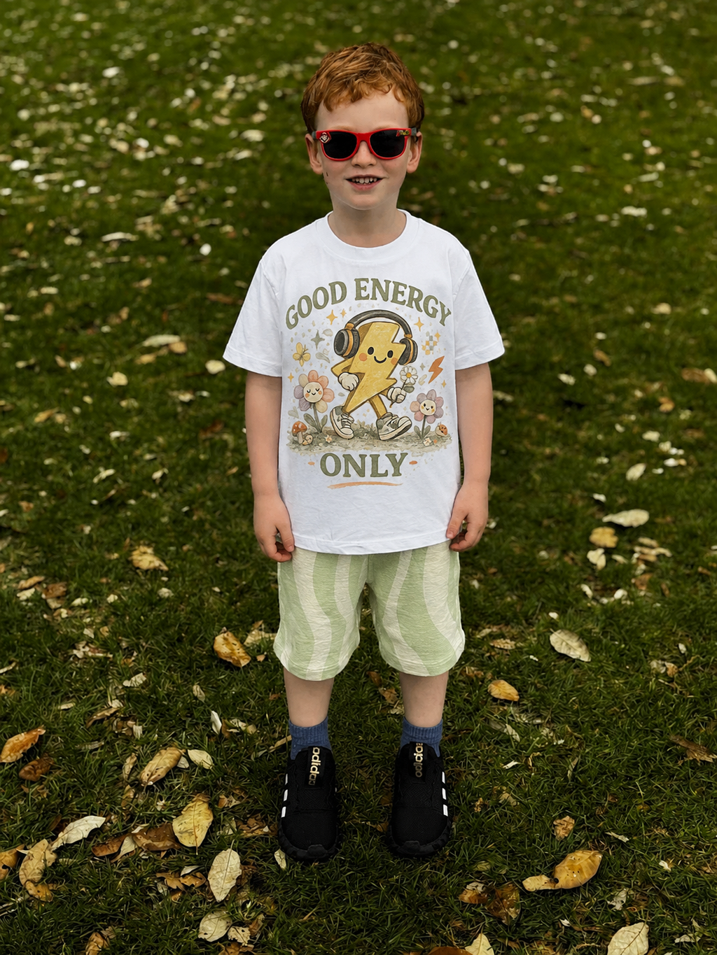 Child wearing a white t-shirt with Good energy only tee design on a grassy background