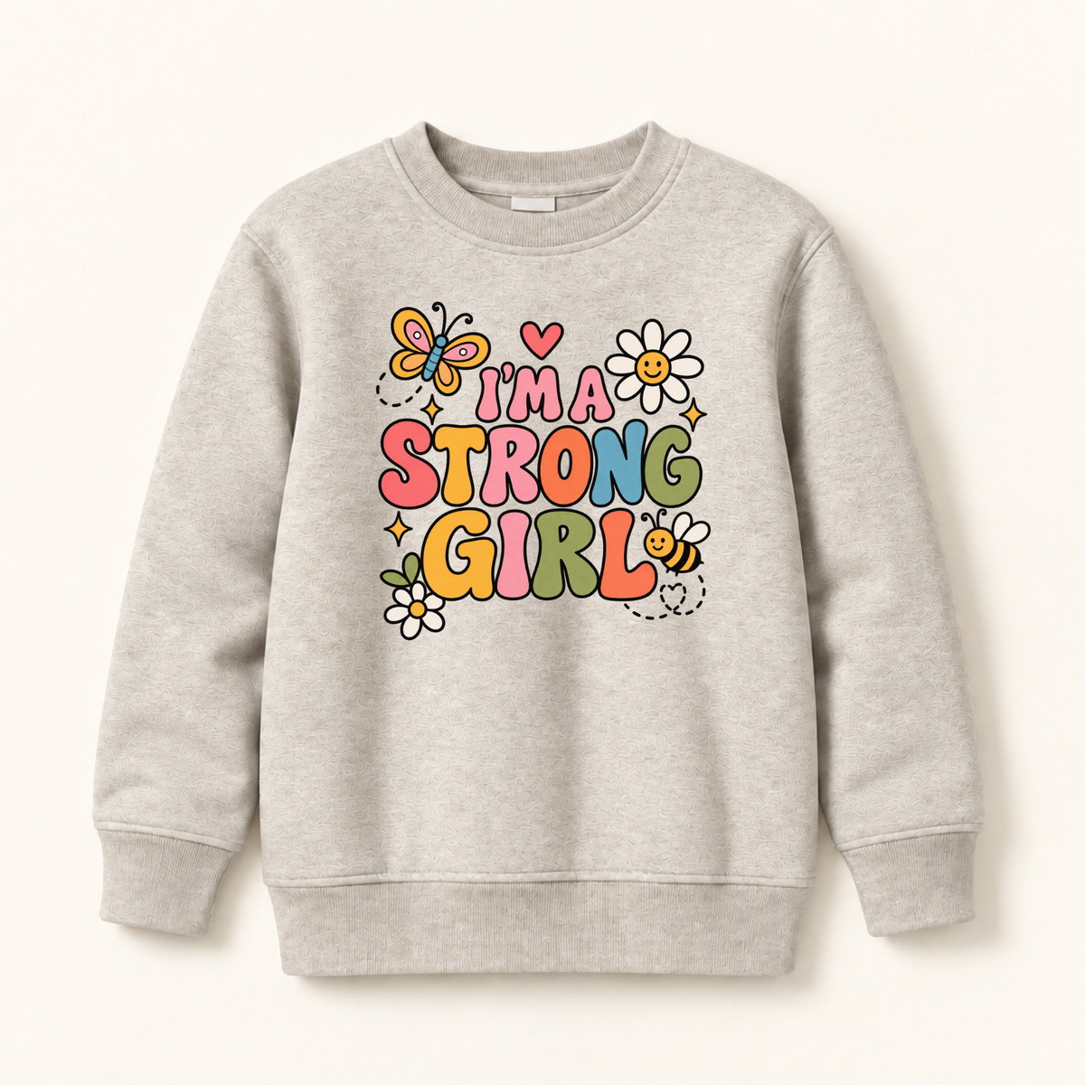 A light heather gray crewneck sweatshirt featuring a colorful graphic print on the front that reads 'I'M A STRONG GIRL' in playful multicolor letters, decorated with cartoon butterflies, flowers, and a bee, shown against a light beige background.