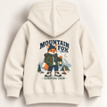 A cream-colored hooded sweatshirt shown from the back, featuring a large graphic print of a cartoon fox dressed in outdoor gear with the text 'MOUNTAIN FOX' and 'CAMPFIRE CREW'.