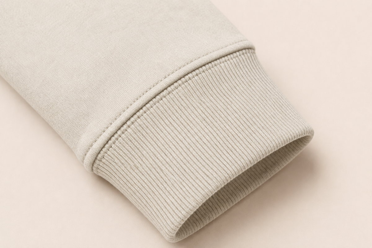 Close-up of a ribbed knit cuff on a light beige or off-white fabric, shown against a matching pale beige background.