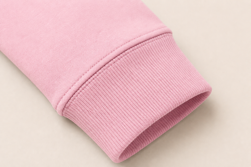 Close-up of a light pink ribbed knit cuff, likely from a sweatshirt or sweater, shown on a plain light beige background.