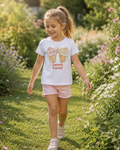Young girl walking in a garden wearing a white t-shirt with sweet Ice cream characters and text.