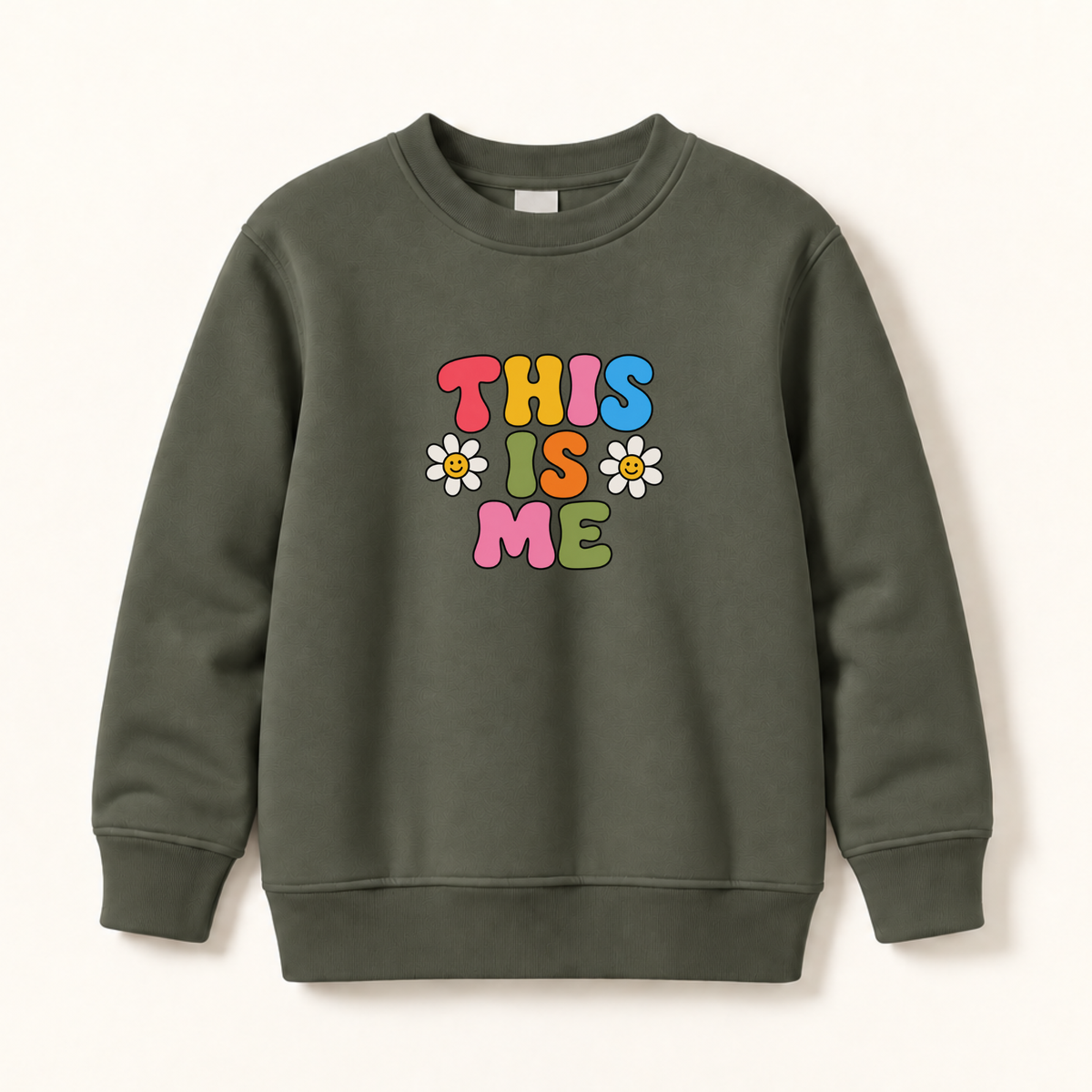 An olive green crewneck sweatshirt featuring a colorful retro graphic that reads 'THIS IS ME' in bubble letters with three small daisy flowers, displayed on a clean off-white background.