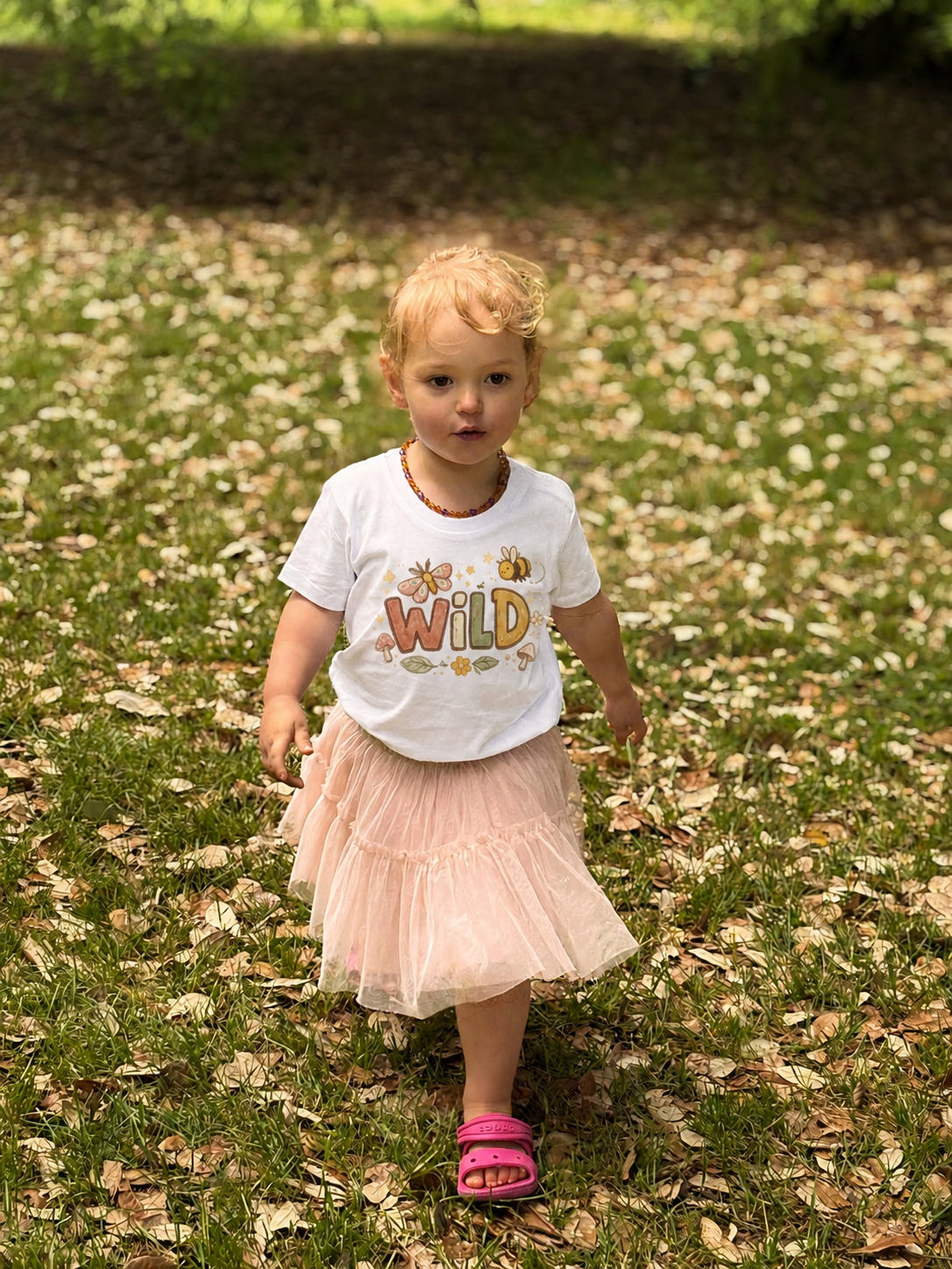 Child wearing a 'Wild' t-shirt in a grassy outdoor setting