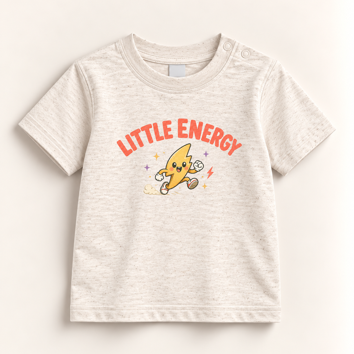 A baby t-shirt in a light heathered cream color, featuring a cartoon graphic of a running yellow lightning bolt character with the text 'LITTLE ENERGY' in orange-red arched above it. The t-shirt is displayed flat against a warm off-white background.