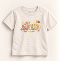 A baby t-shirt in a light heathered cream color, featuring a colorful graphic on the chest with the word 'WILD' in earthy tones, accompanied by a butterfly, a bee, and small mushrooms.